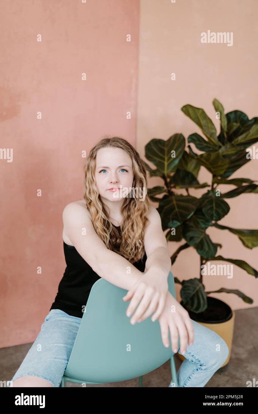 Wunderschöne junge Frau, die direkt in die Kamera starrt und auf einem Stuhl sitzt Stockfoto