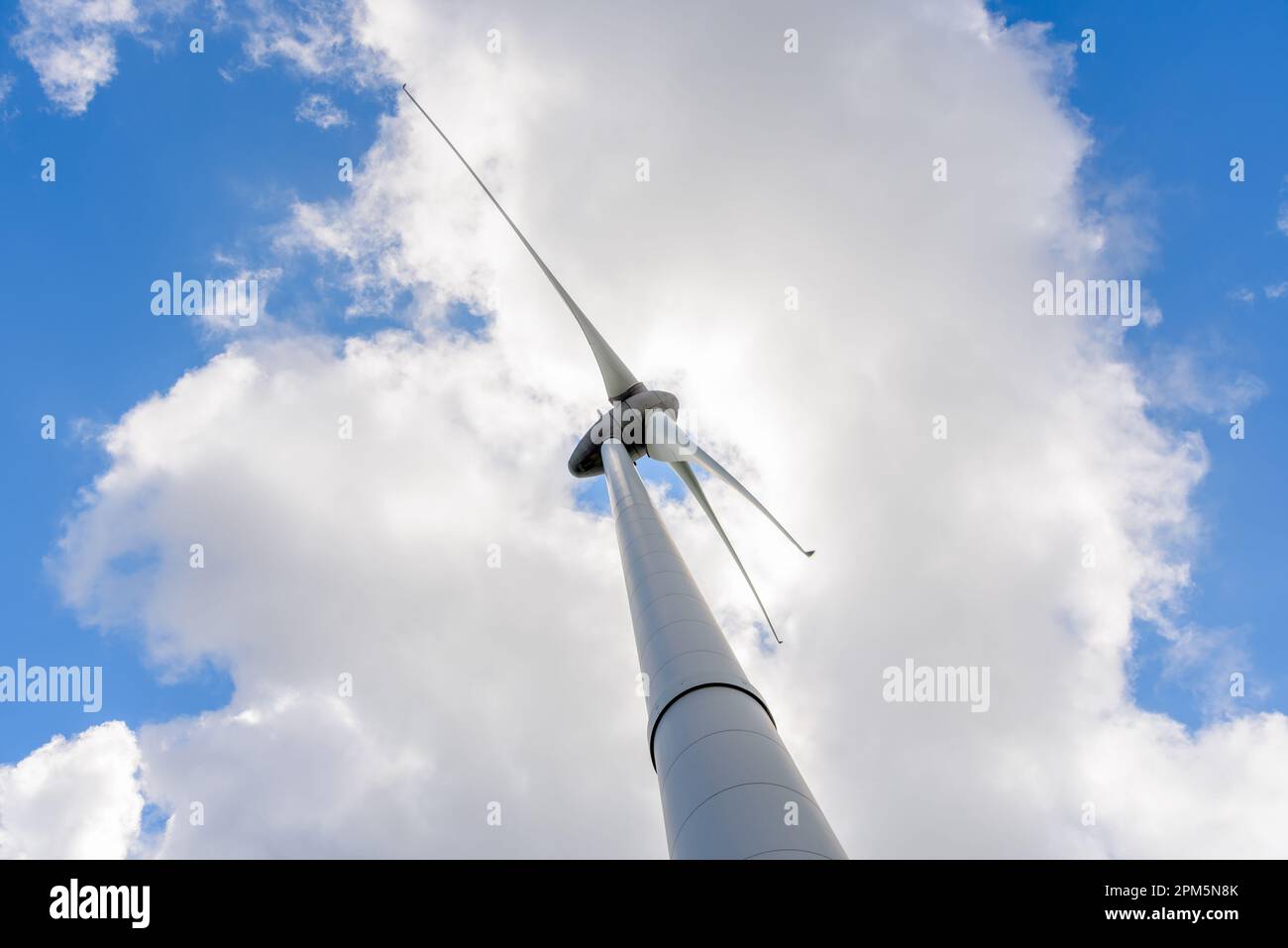 Blick von unten auf eine Windturbine vor blauem Himmel mit Wolken im Sommer Stockfoto