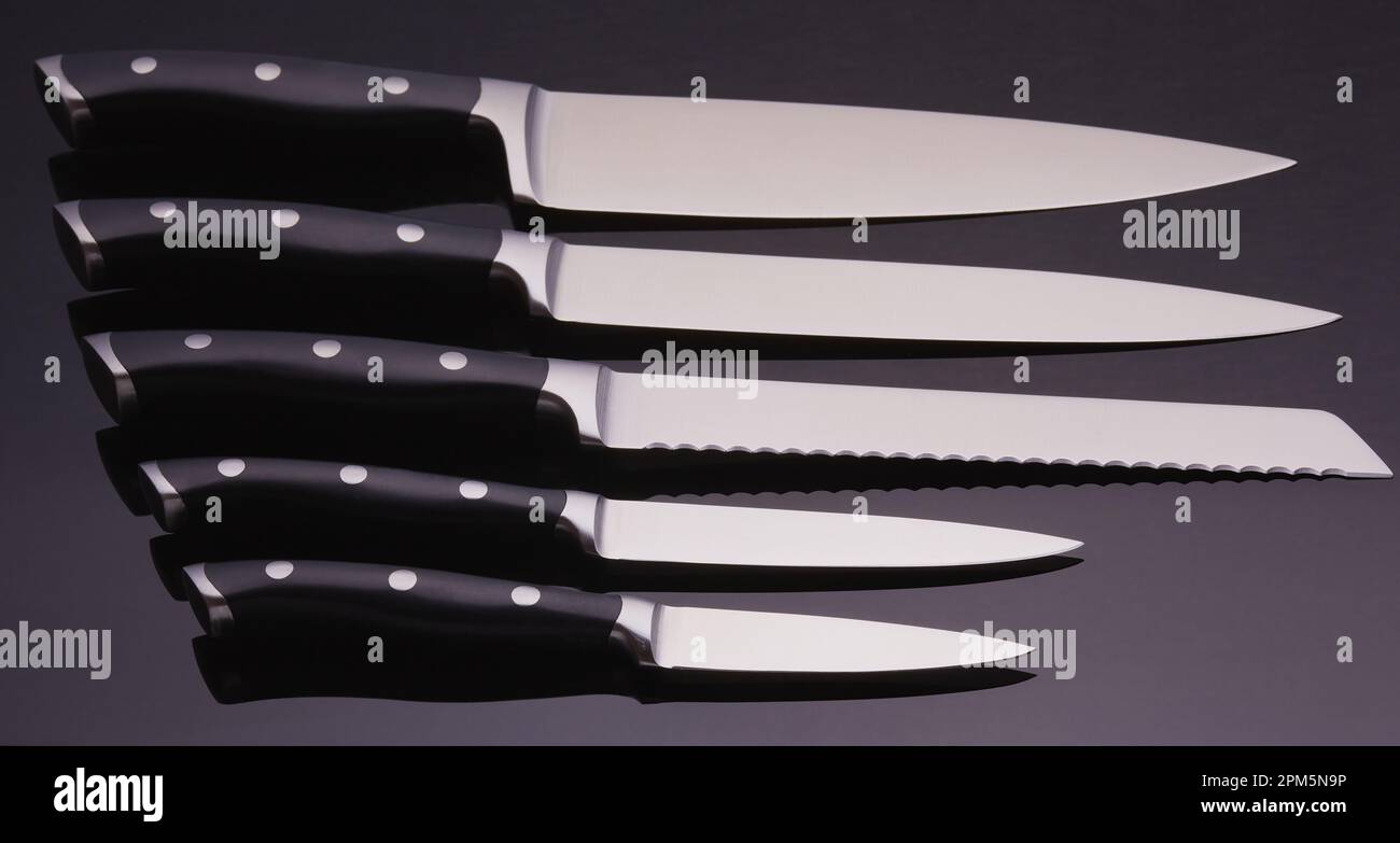 Komplettes Set von Küchenmessern auf schwarzem Hintergrund mit einem Gradienten über den Klingen. Stockfoto