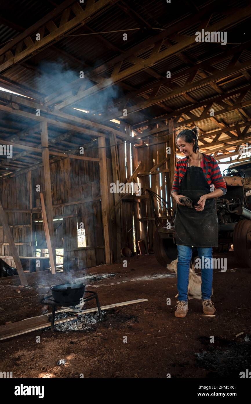 Die junge Frau in Uniform, die in einer Fabrik arbeitet, die für alle kocht, mit Feuer auf dem Boden. Stockfoto