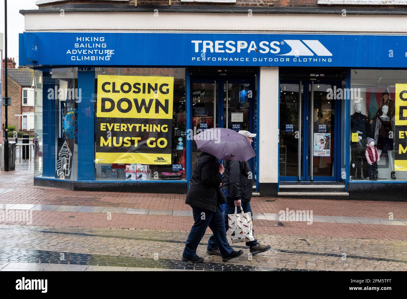 Menschen in Southend auf der Sea High Street mit Sonnenschirmen, vorbei an der Schließung des Hausfriedensbekleidungsgeschäfts. Regnerischer Feiertag am Montag. Mühsamer Laden Stockfoto