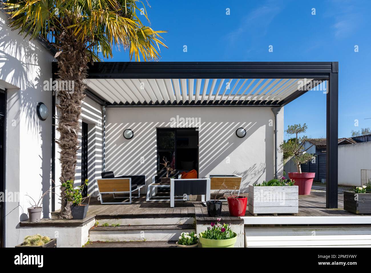 Trendige Terrasse Pergola Schatten Struktur, Markise und Terrasse Dach, Gartenlounge, Stühle, Metall-Grill umgeben von Landschaft Stockfoto