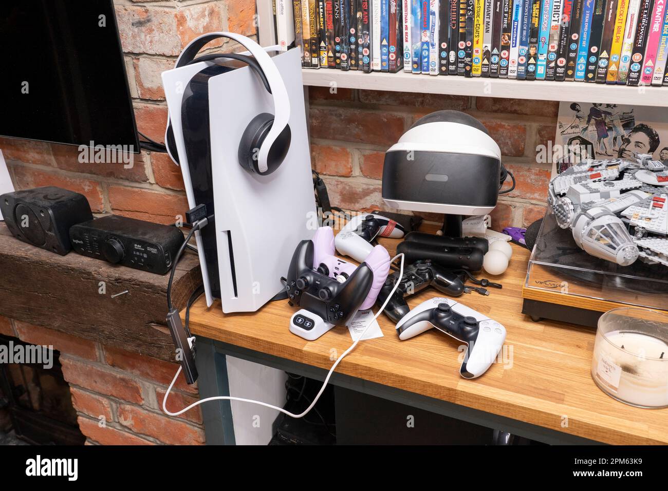 Eine Sony PlayStation 5 Heimvideospielkonsole mit Controller zum Aufladen, über-Ohr-Kopfhörer und ein Virtual Reality VR-Headset in einer britischen Lounge Stockfoto