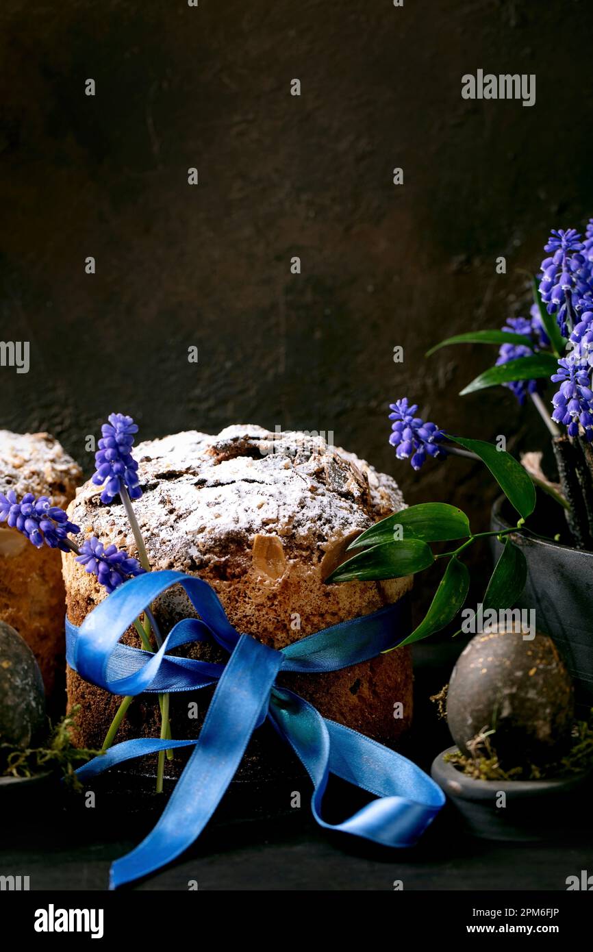Hausgemachter traditioneller Osterpanettone-Kuchen mit farbigen schwarzen Eiern und blühenden Muscari-Blumen auf einem schwarzen Holztisch. Traditionelles italienisches Ostergebäck, Stockfoto