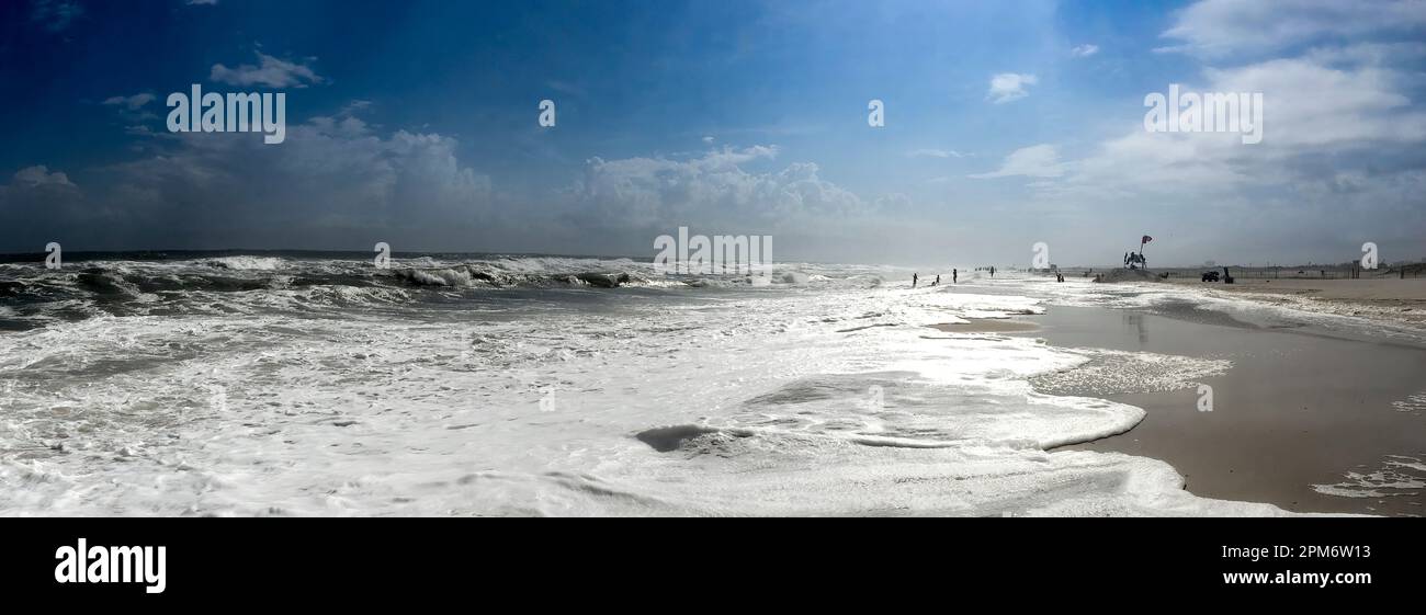 Strand, Spätnachmittag, sanfte Wellen und Sandstrand, blauer Himmel mit weichen Wolken, Bademeister Stuhl, Leute in Silhouette in der Ferne. Panorama. Stockfoto