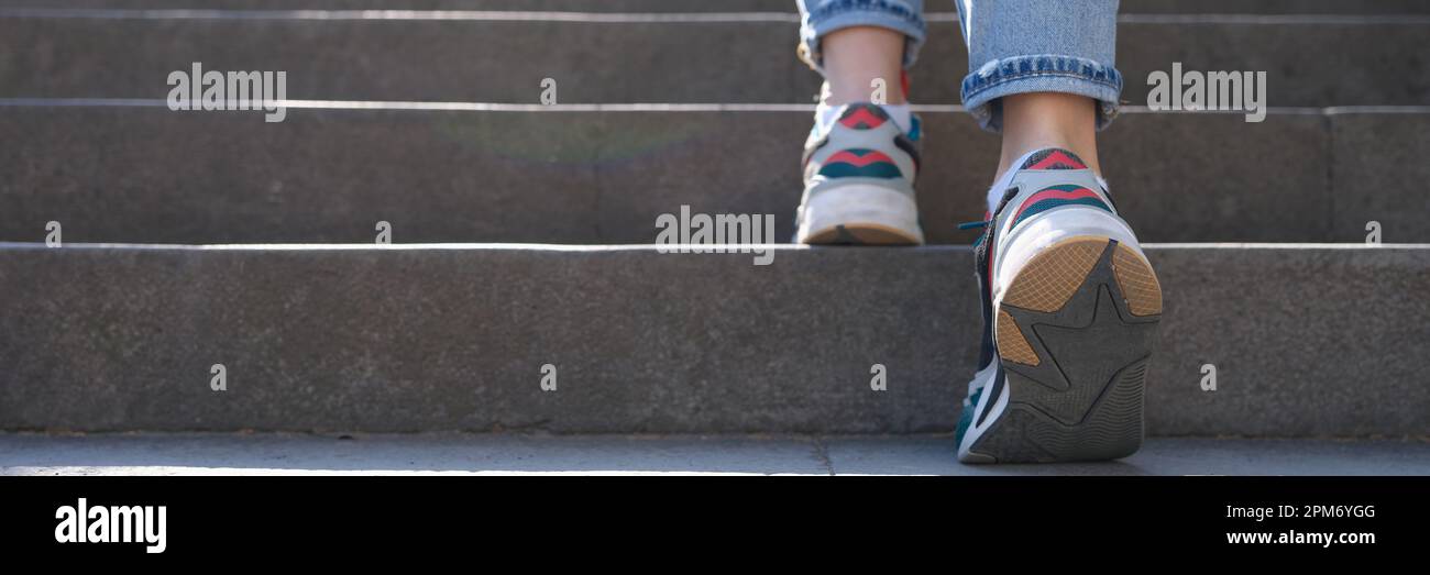 Frau in Jeans und Sneakers, die steile Treppen hochsteigt Stockfoto