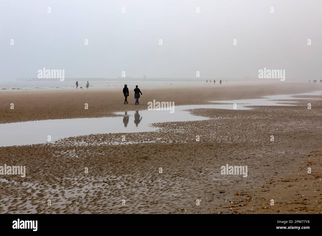 Besucher von Camber Sands, die an einem nebligen Ostersonntagmorgen am Strand spazieren gehen. Stockfoto