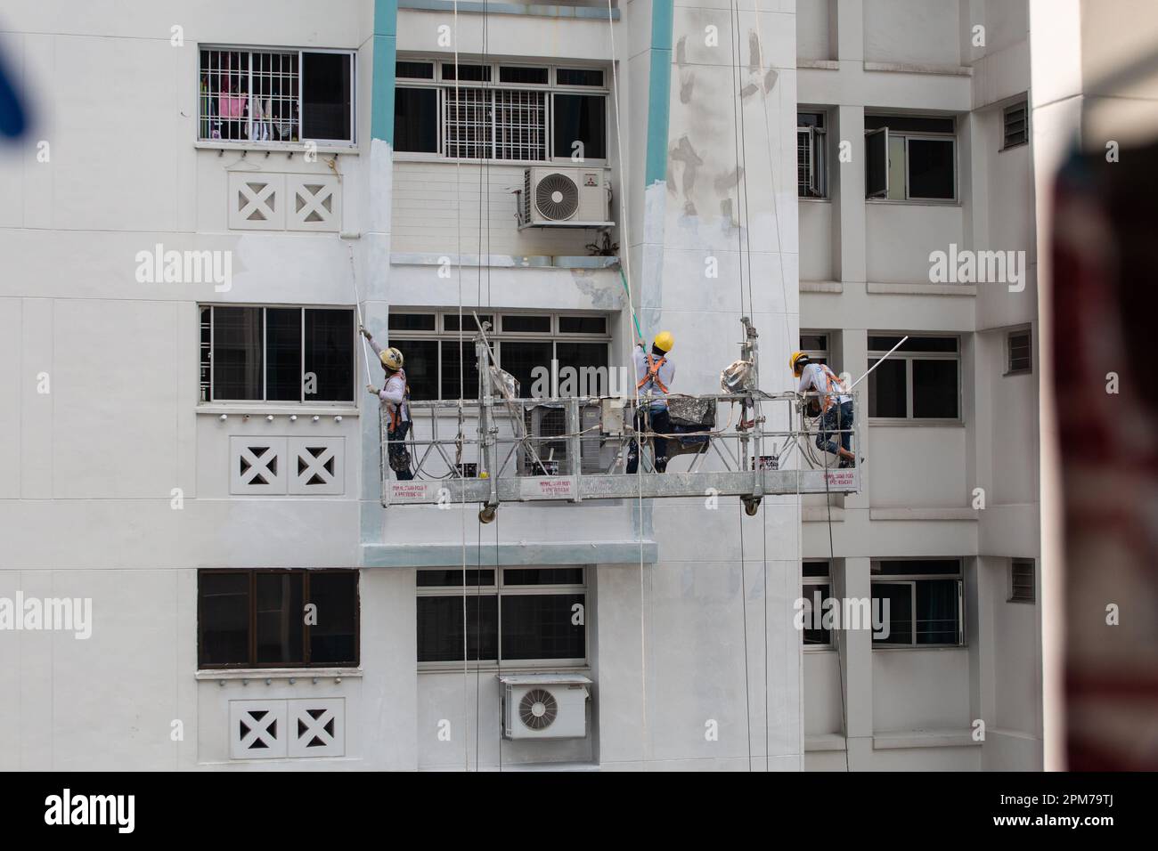 Drei Arbeiter auf den Gerüstaufzügen in der Höhe, die ihr Bestes tun, um Schälfarbe abzukratzen und neue Farbe auf der Fassade des Gebäudes zu beschichten. Stockfoto