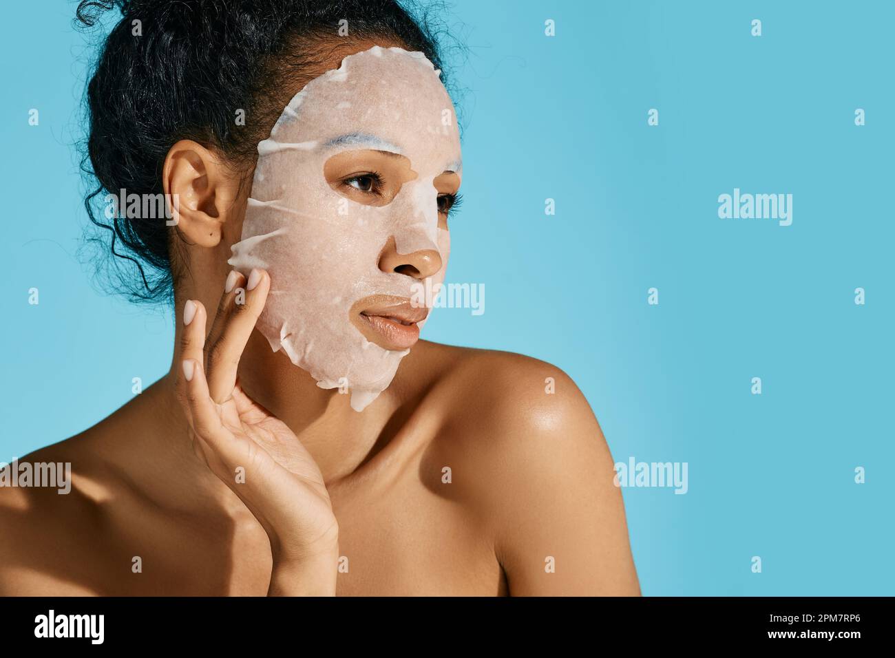 Gesichtshydratisierungs- und Verjüngungsverfahren. Afroamerikanische Frau mit feuchtigkeitsspendender Hautpflegemaske auf blauem Hintergrund, hohe Qualität Stockfoto