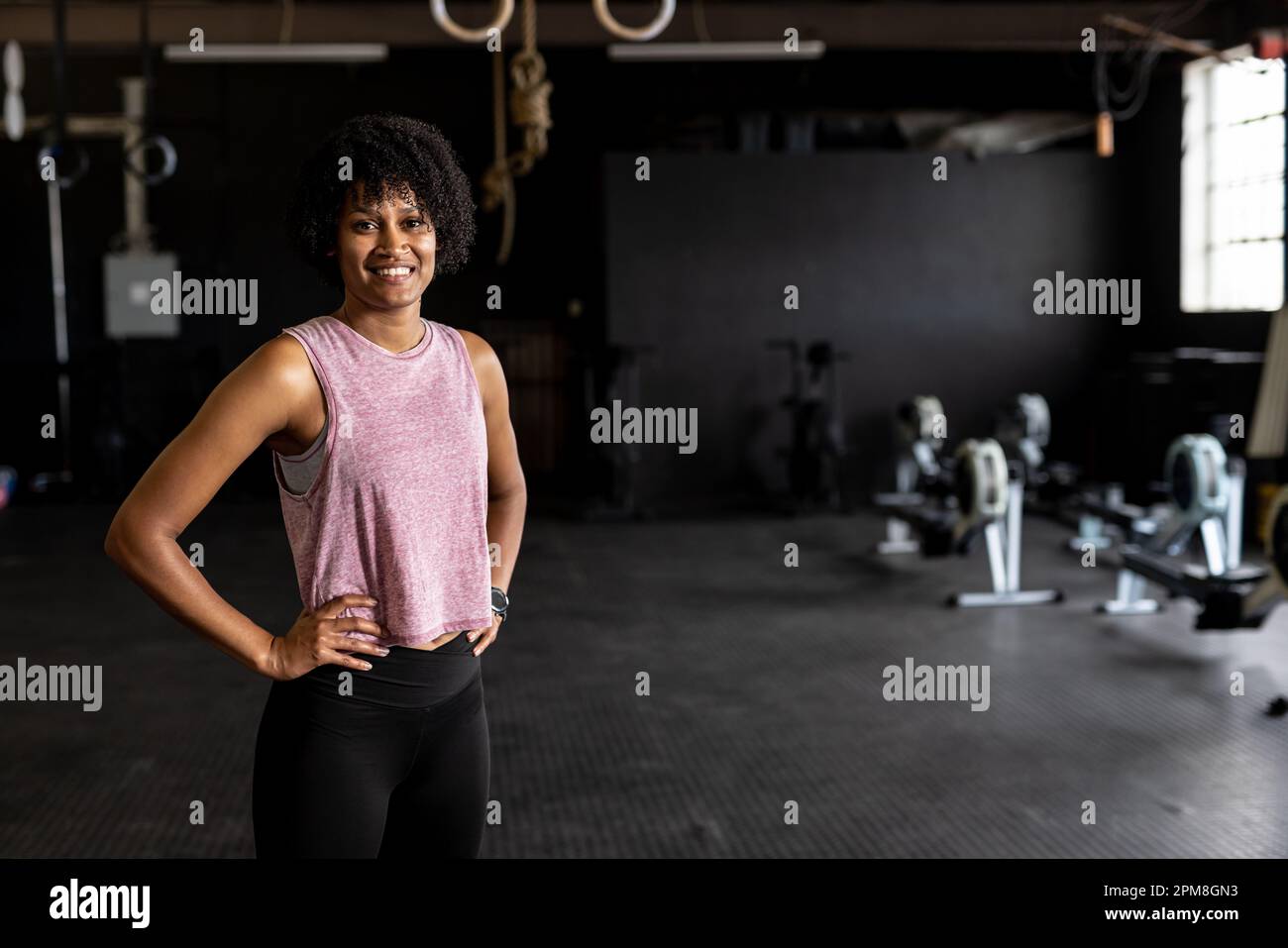 Porträt einer birassischen selbstbewussten jungen Frau mit Armen Akimbo im Fitnessstudio Stockfoto