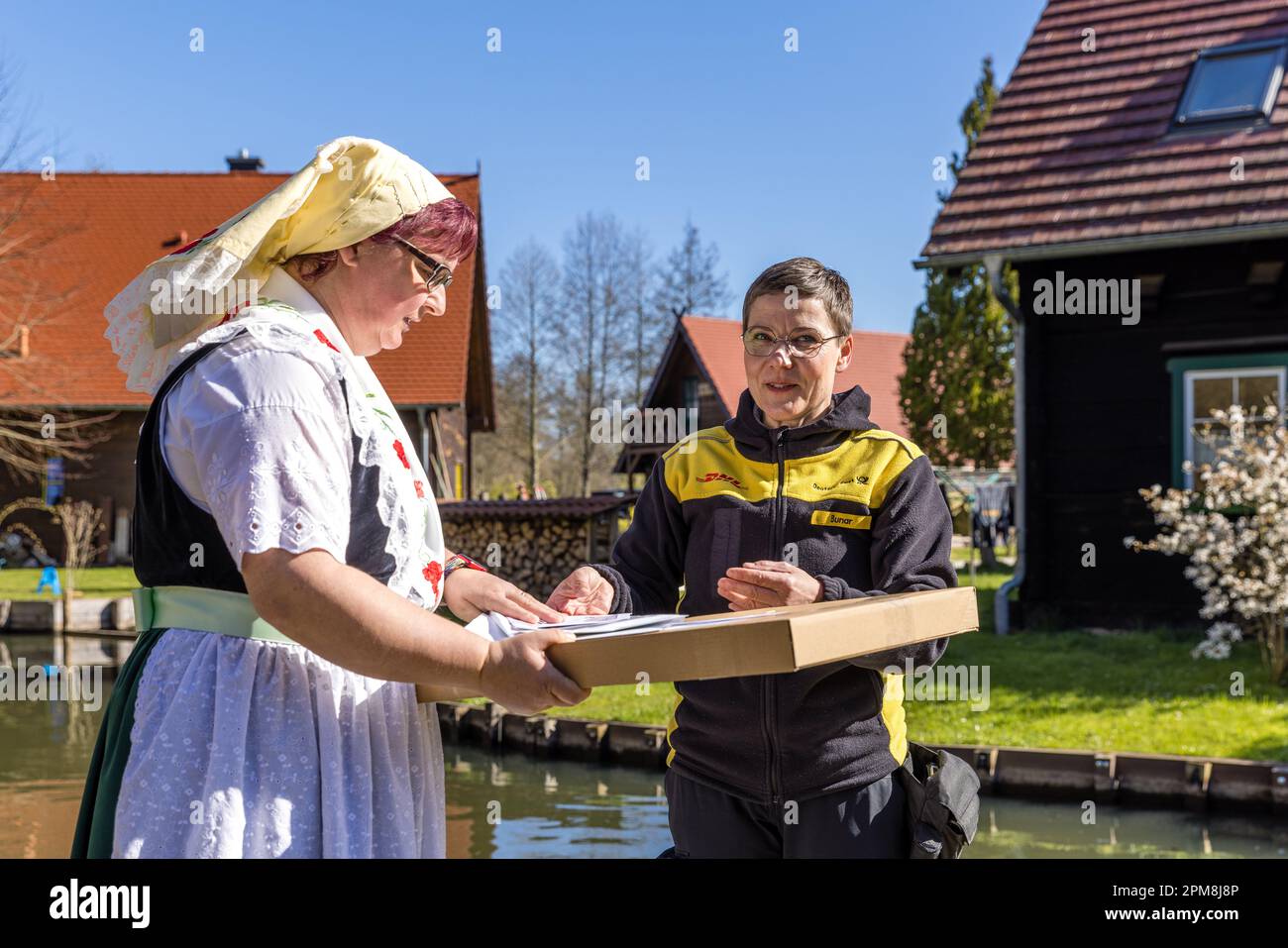 12. April 2023, Brandenburg, Lübbenau/OT Lehde: Andrea Bunar übergibt ihre Post an die Barge Ferrywoman Birgit Schneider, die in traditionellem Spreewaldkostüm gekleidet ist. Der Postbote Bunar, für den dies bereits ihre zwölfte Saison auf dem Wasser ist, liefert wieder einmal Briefe und Pakete auf dem Wasserweg im Spreewalddorf Lehde aus. Viele Haushalte hier haben keine direkte Verbindung zur Straße. (Zu dpa "Postfrau Bunar stakt los - Post kam im Spreewald wieder per Kahn") Foto: Frank Hammerschmidt/dpa Stockfoto