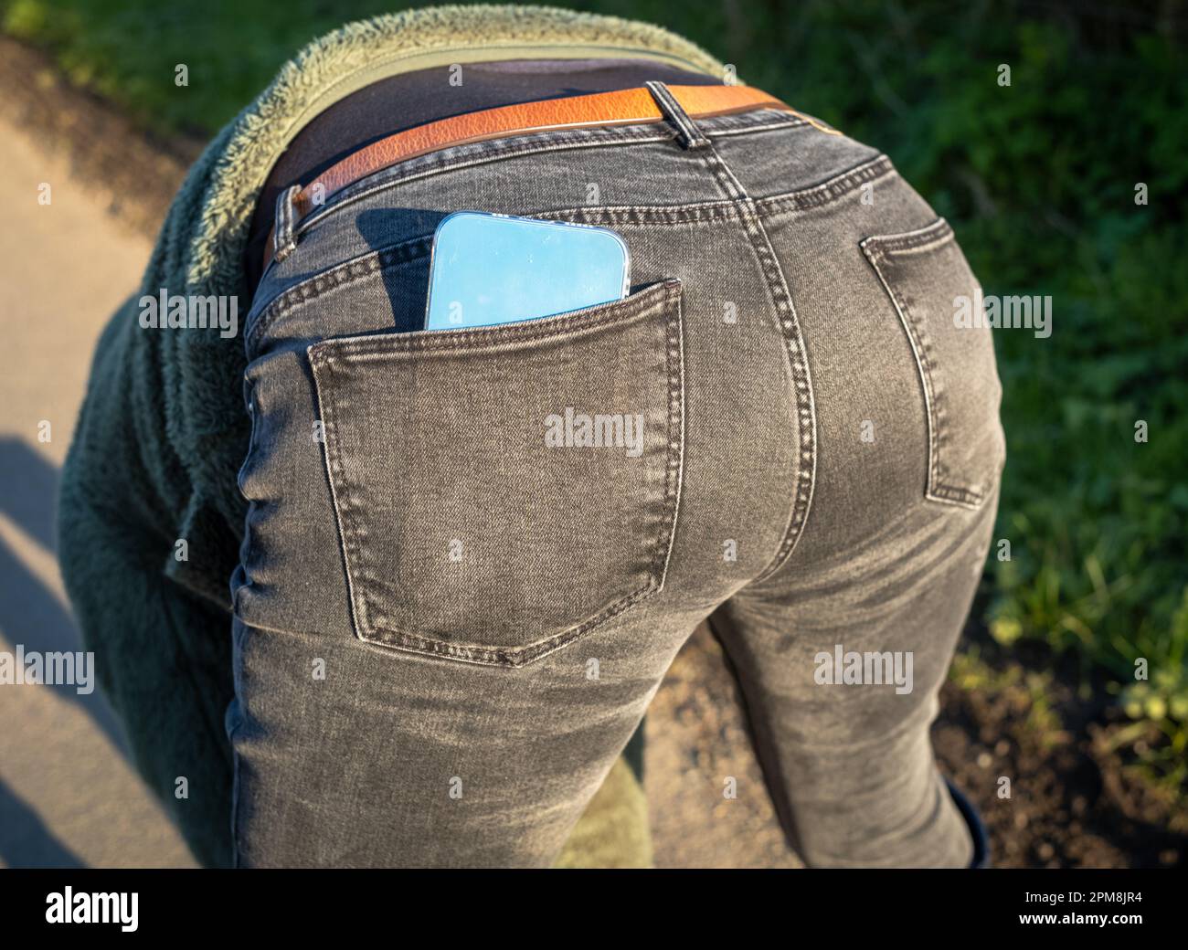 Eine Frau, die ein Handy in der Hosentasche ihrer Jeans trägt, beugt sich um. Stockfoto