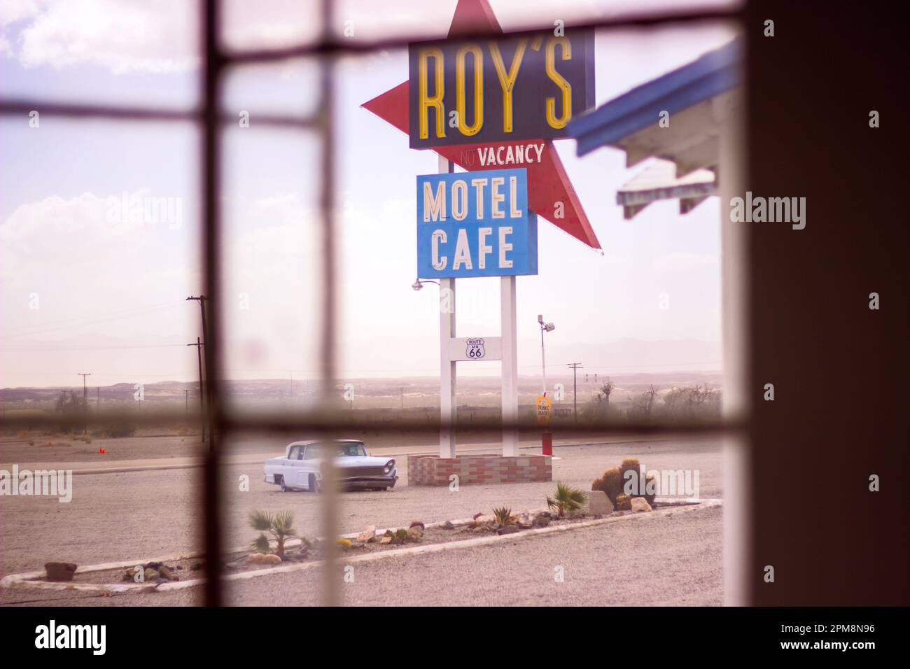 Dieses gespenstische Foto zeigt die trostlose Schönheit eines verlassenen Motelzimmers in Amboy, Kalifornien, mit dem ikonischen Schild von Roy's Motel und einem sichtbaren Auto Stockfoto