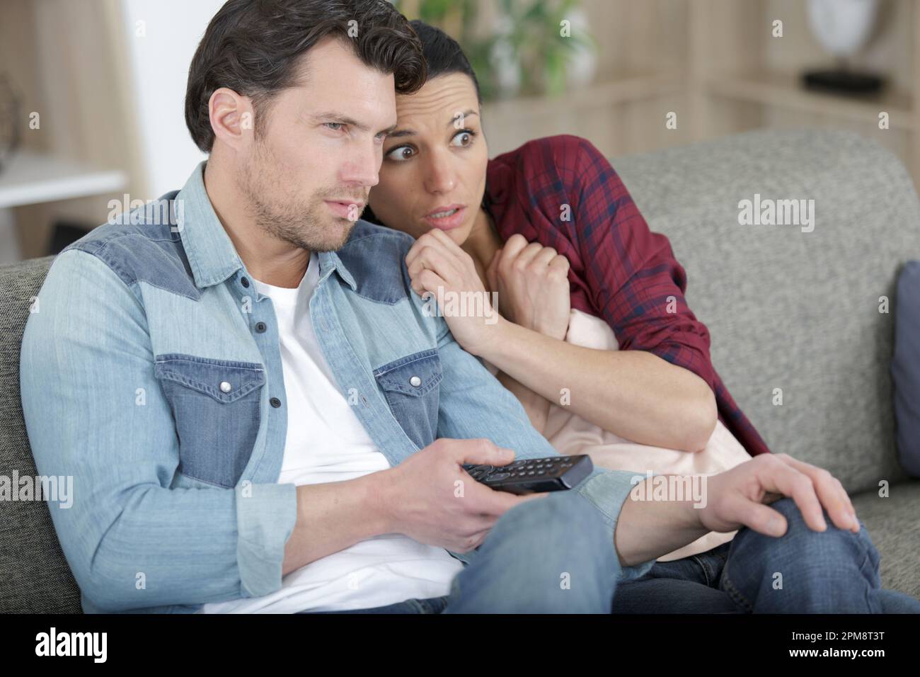 Ein Paar, das auf der Couch sitzt und sich einen Horrorfilm ansieht Stockfoto