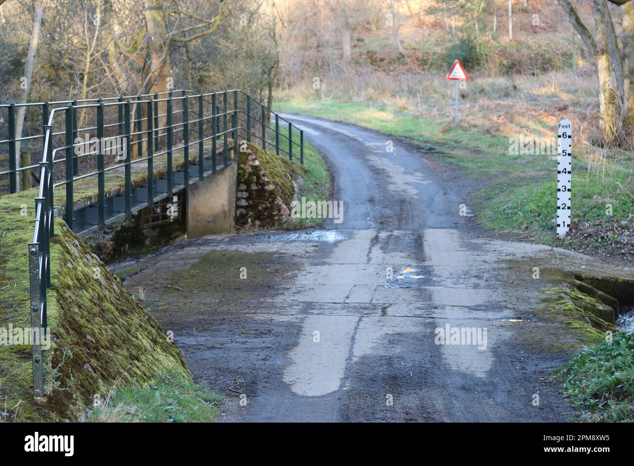 Straße über einen Fluss ford mit einem großen Schild zur Messung der Wassertiefe und Fußgängerbrücke Stockfoto
