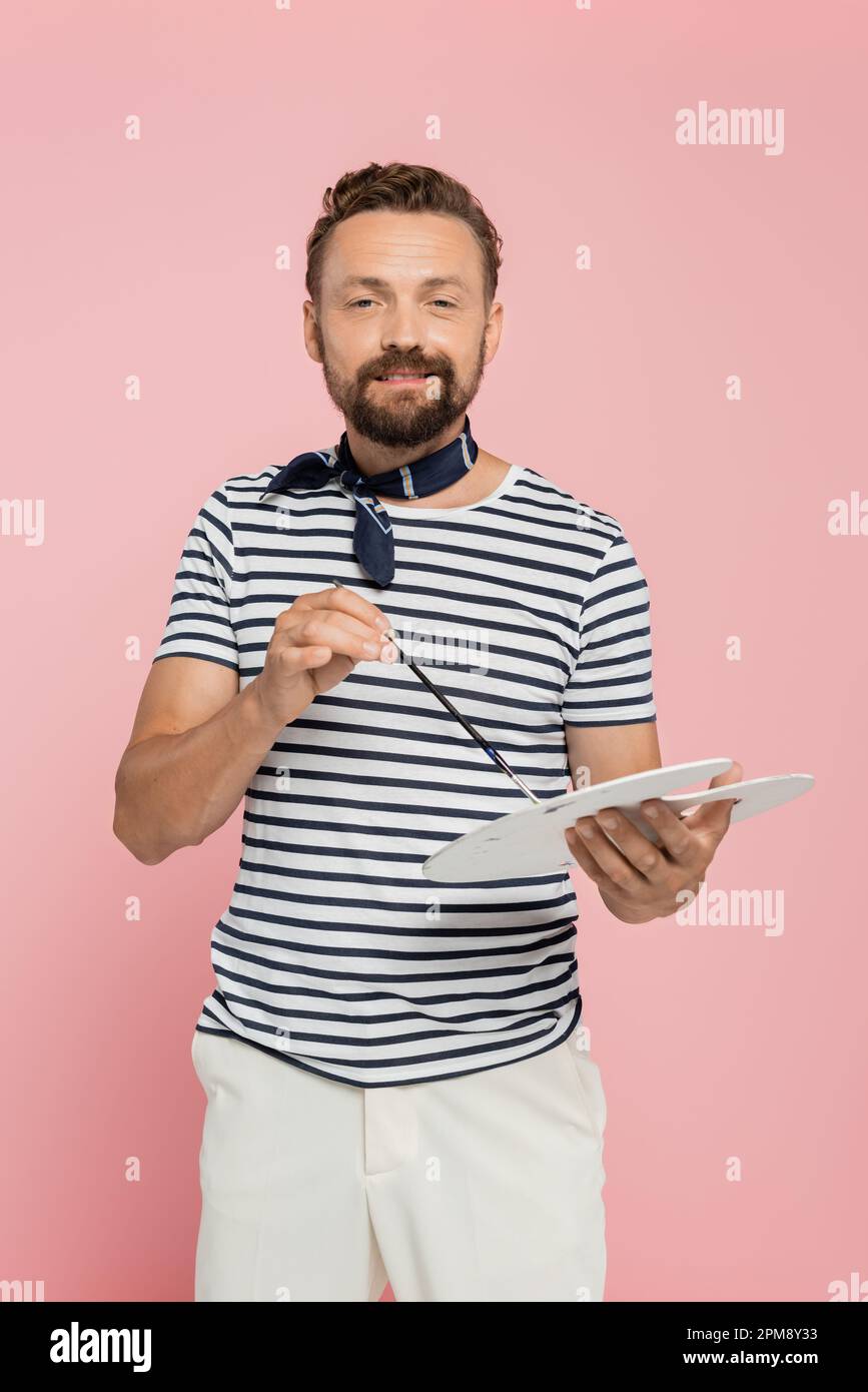 Fröhlicher französischer Künstler mit Halstuch und Pinsel auf pinkfarbenem Stockbild Stockfoto