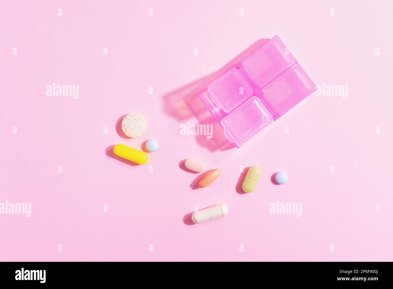 Rosafarbener Pillen-Organisator mit bunten Pillen und Nahrungsergänzungsmitteln auf pinkfarbenem Hintergrund, Draufsicht. Stockfoto