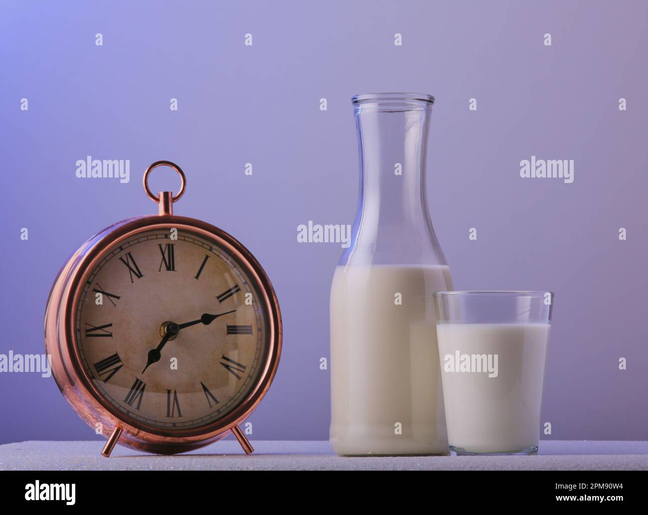 Milchkanne und ein Glas Milch neben einem Wecker für die Morgenzeit. Stockfoto