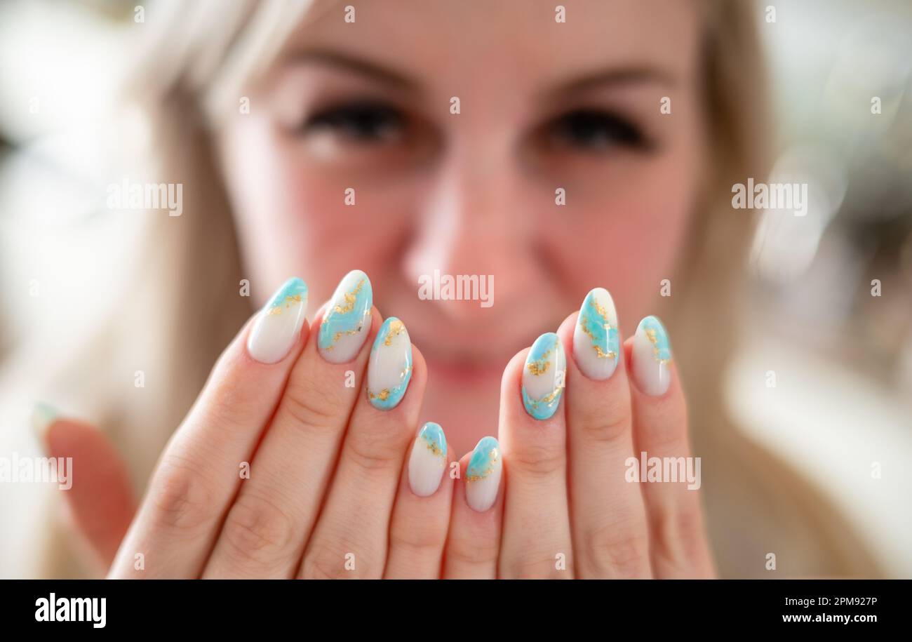 Hübsche Fingernägel nach der Maniküre mit lächelnder blonder Frau im Hintergrund (Acrylnägel, Gelnägel) Stockfoto