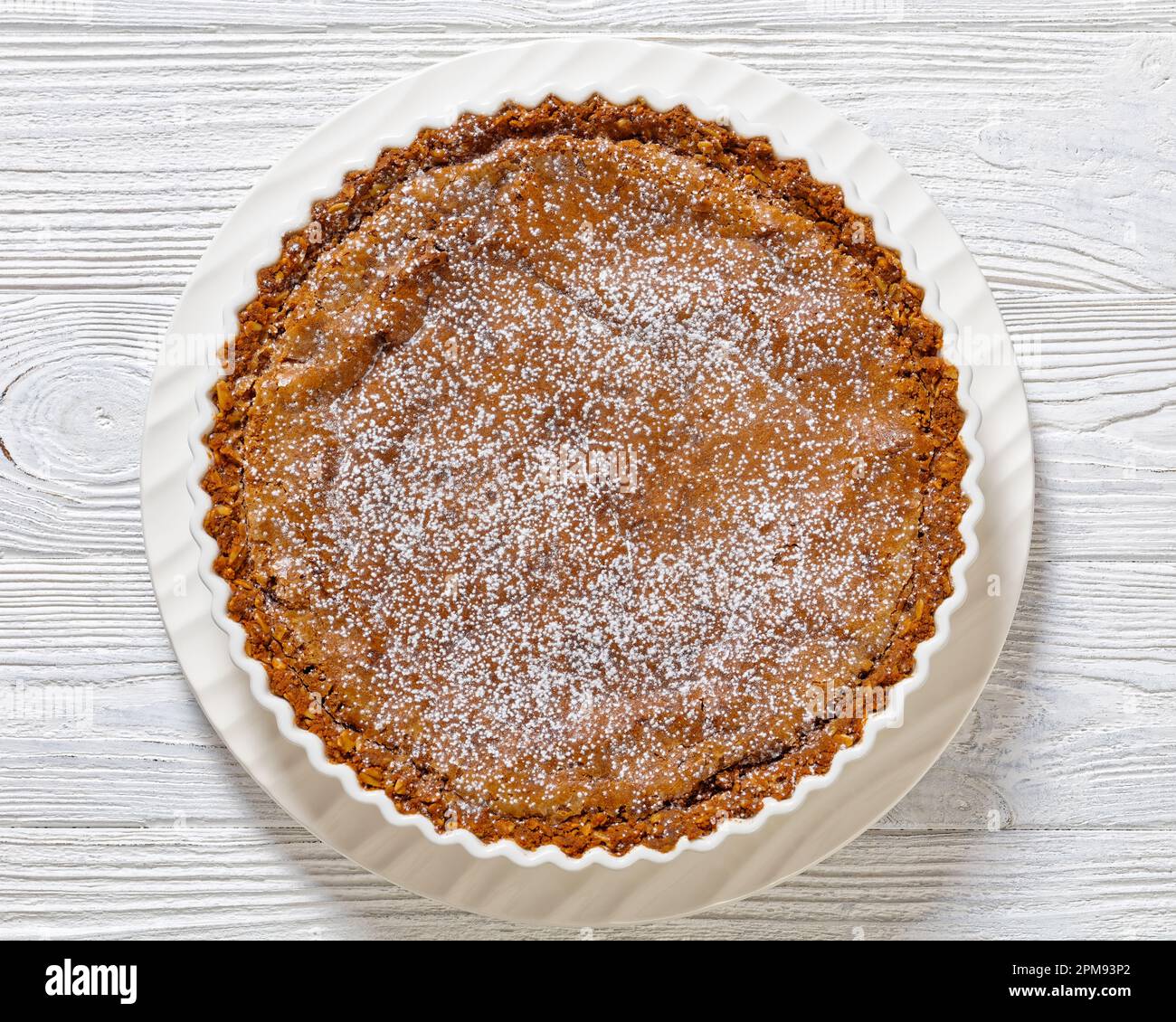 Momofuku Milk Bar Crack Pie mit knuspriger Haferkruste und leckerer Füllung, gefüllt mit Süßwaren, weißer Backform auf weißem Holztisch, horizontal Stockfoto