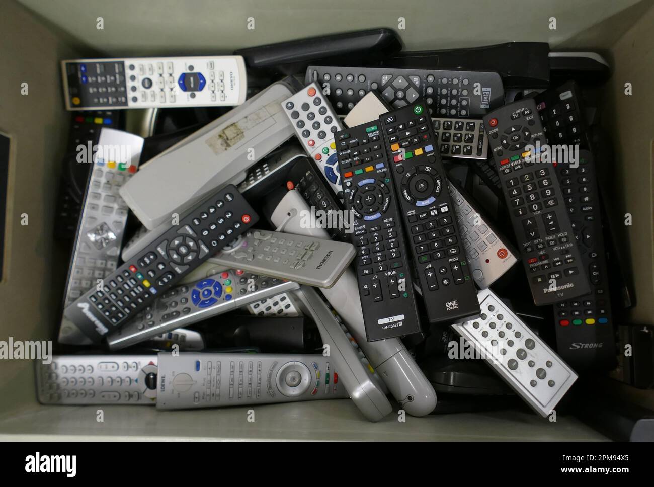 Verwarfene Fernsehfernbedienungen in einer Kiste. Visuelle Metapher für elektronischen Abfall, E-Waste-Recycling, Konsumverhalten und nachhaltiges Ressourcenmanagement. Stockfoto