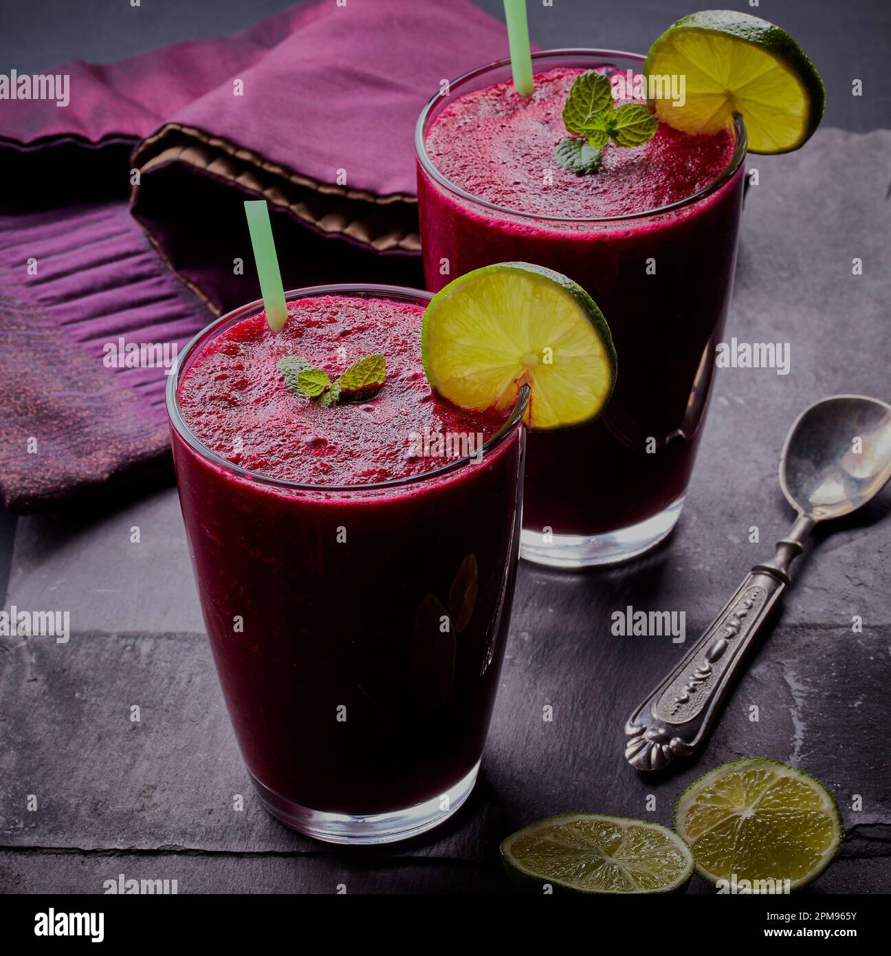 Gesunde entgiftende lila Smoothie-Getränke garniert mit Limettenscheiben und Minze mit grauem Schieferhintergrund. Stockfoto