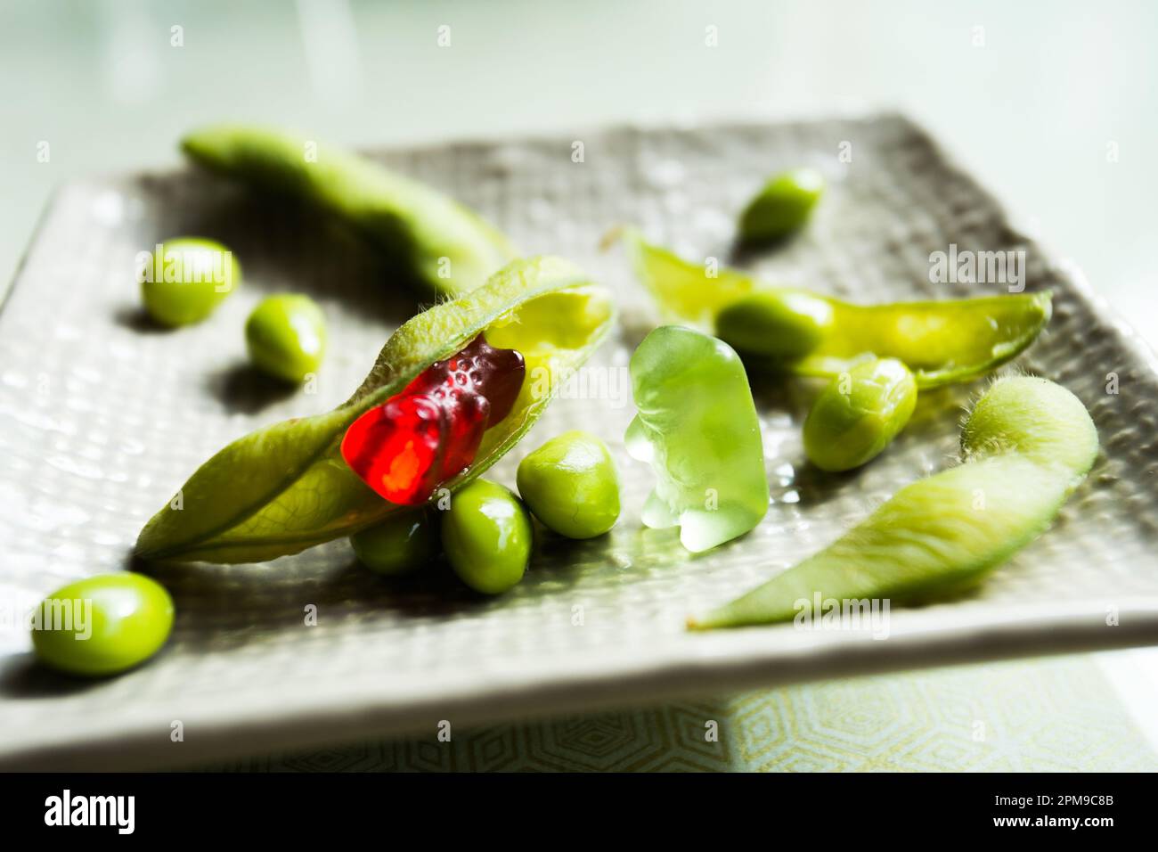 Gummibären, die mit Edamamabohnen auf einem Esstisch spielen. Stockfoto
