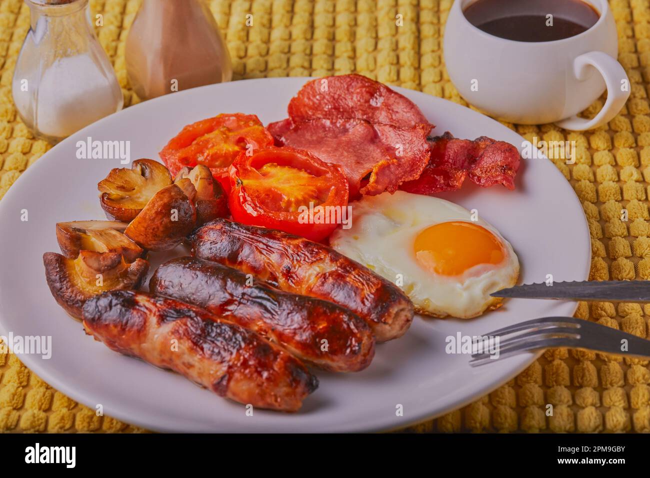 Warmes Frühstück mit Wurst, Speck, Pilzen, Tomaten und Spiegelei mit einer Tasse Kaffee. Stockfoto