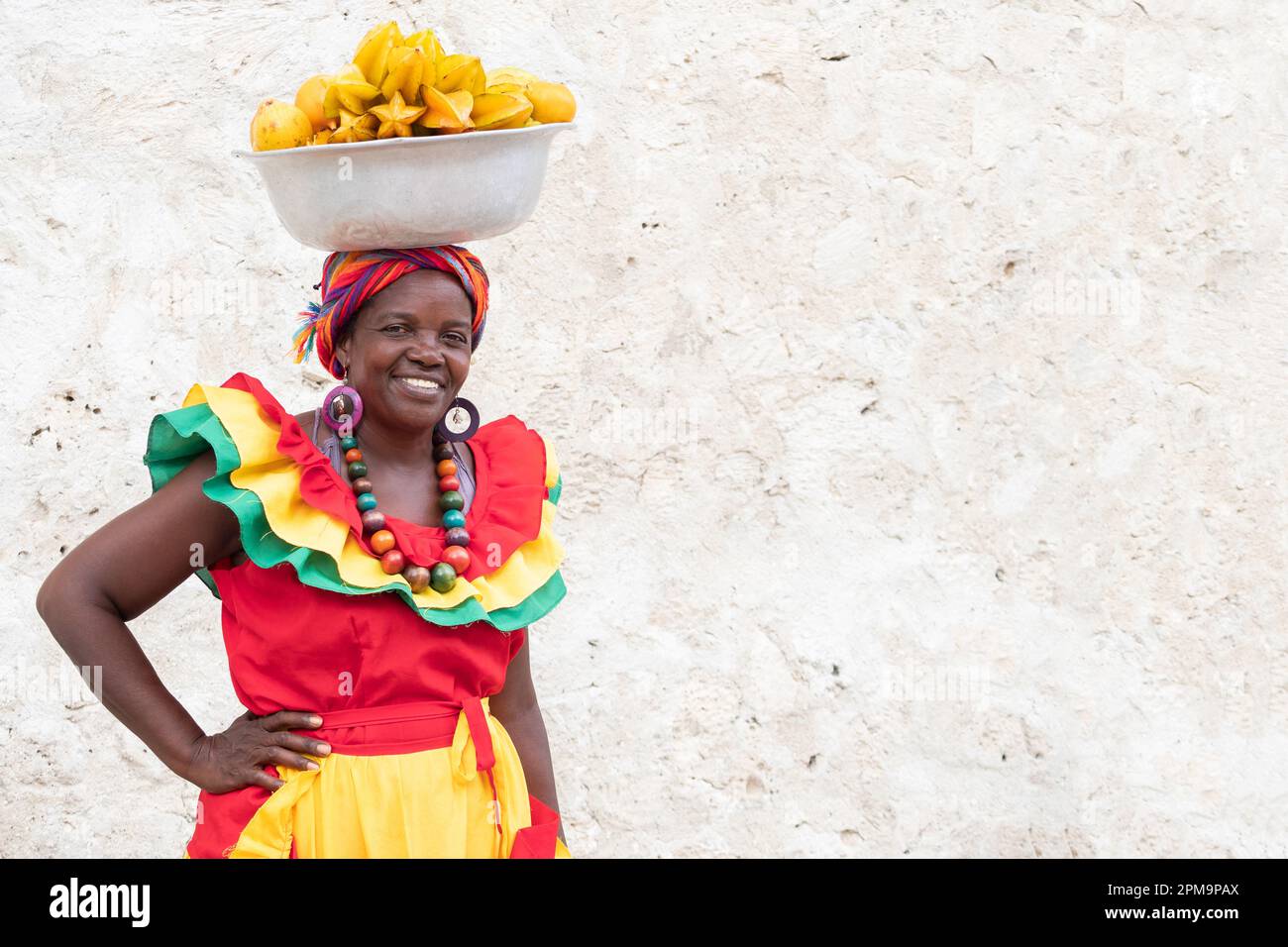 Fröhlicher, lächelnder Palenquera-Straßenverkäufer mit frischem Obst in der Altstadt von Cartagena, Kolumbien. Fröhliche afrokolumbianische Frau in traditionellen Kostümen. Stockfoto