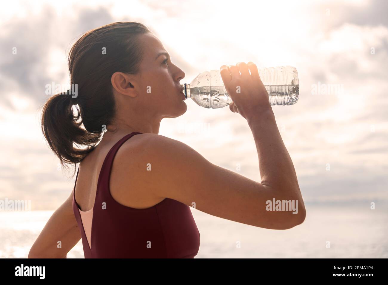 Sportliche Frau, die Wasser aus einer Flasche trinkt, nachdem sie draußen war oder gelaufen ist. Stockfoto
