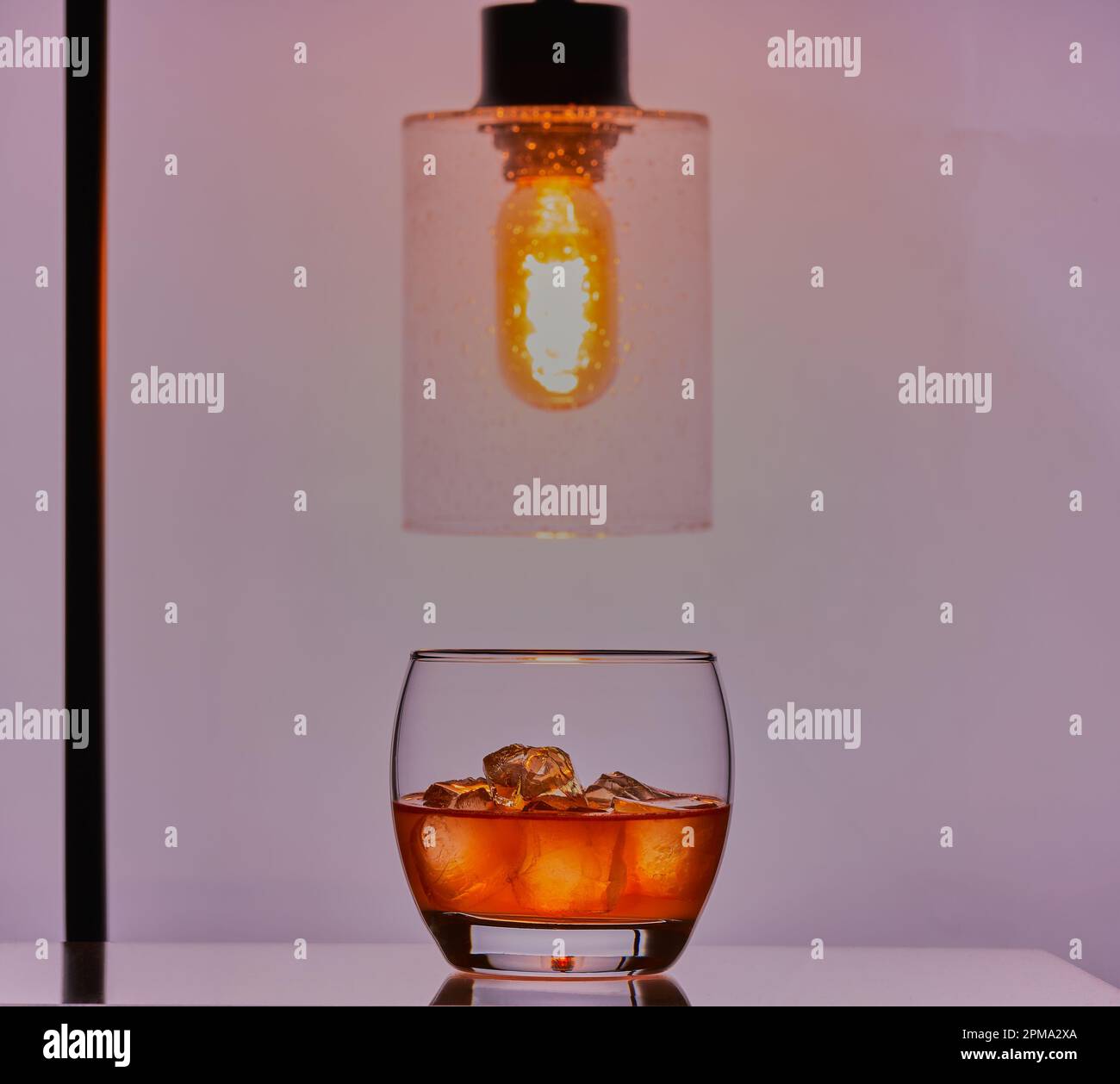 Whisky mit Eis in einem Glas mit einer Lampe darüber, die das Glas beleuchtet. Stockfoto