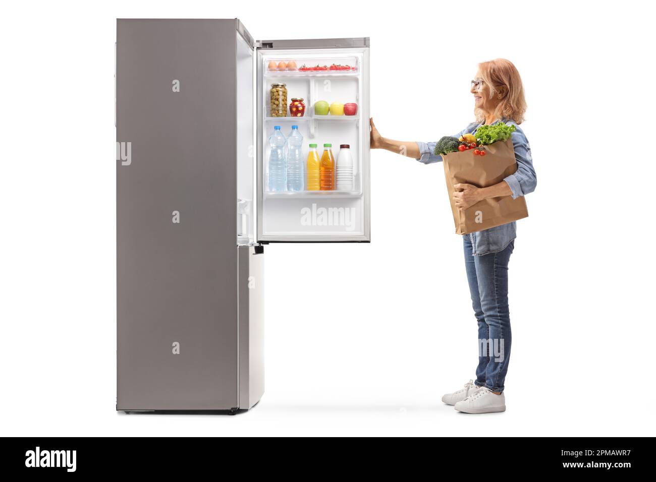 Eine Frau mit einer Einkaufstasche, die einen Kühlschrank öffnet, isoliert auf weißem Hintergrund Stockfoto