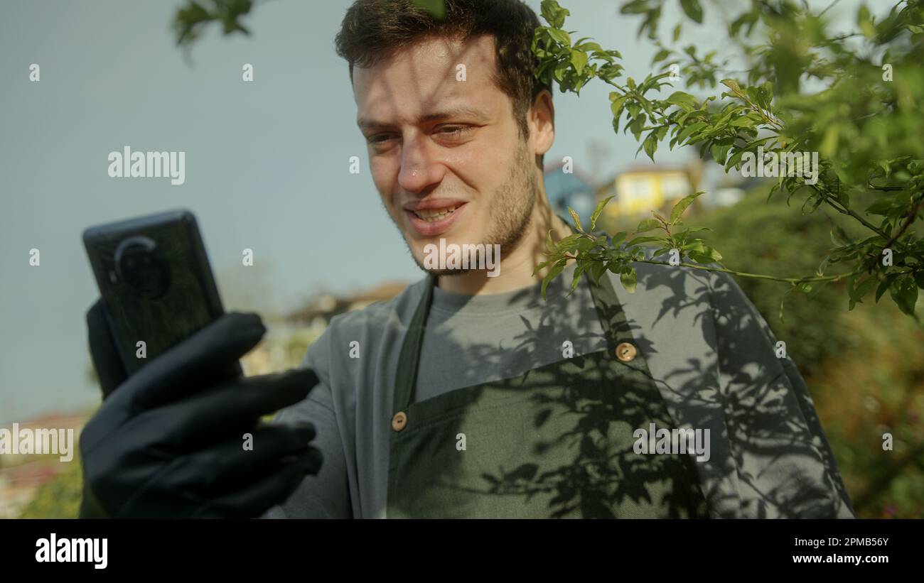 Junger, gutaussehender Bauer oder Gärtner, der draußen mit seinem Telefon in der Hand telefoniert Stockfoto