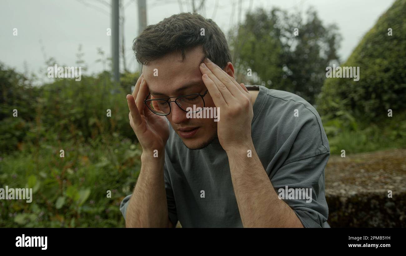 Junger Mann mit Brille kreist in Schmerzen, kämpft mit einem plötzlichen Auftreten von gesundheitlichen Problemen Stockfoto