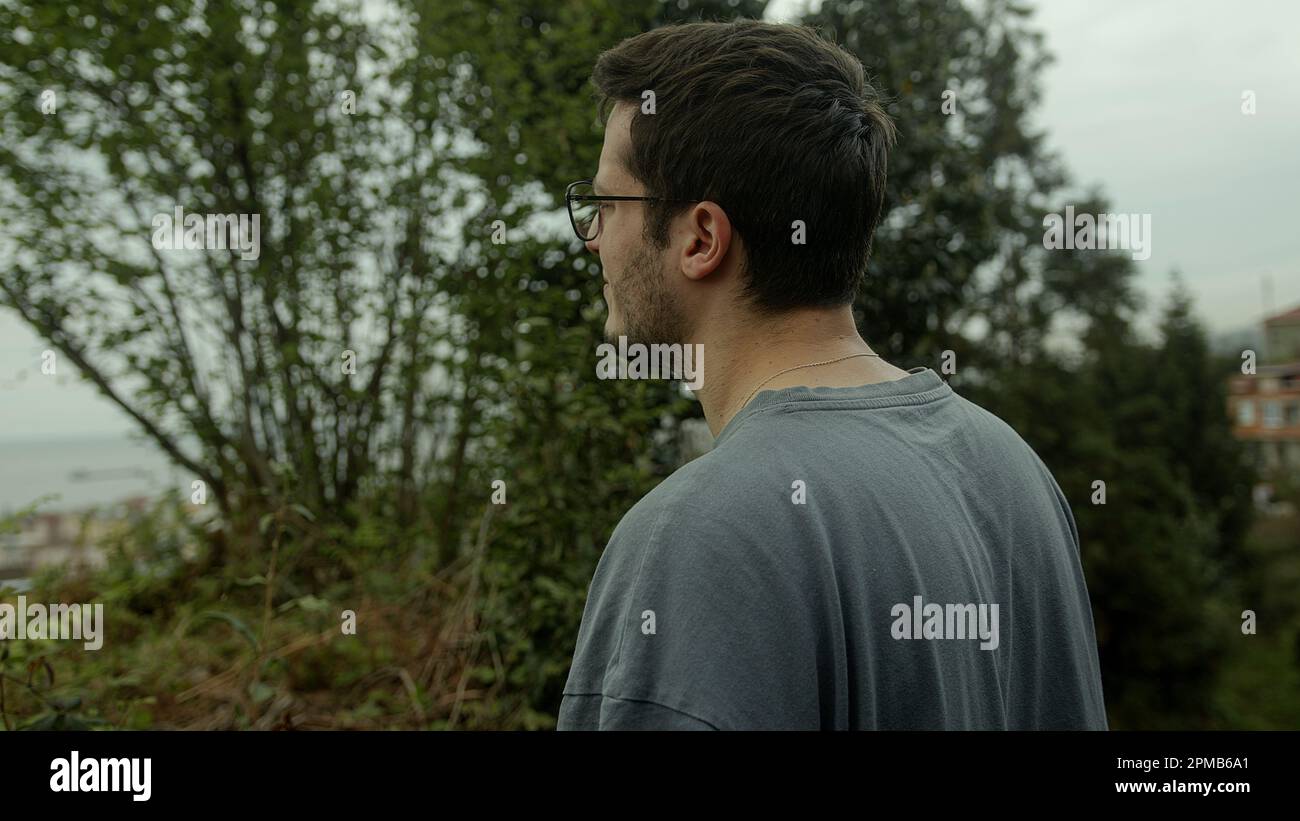 Junger brünetter Mann mit Brille auf einem Spaziergang im Wald - Rückansicht Stockfoto