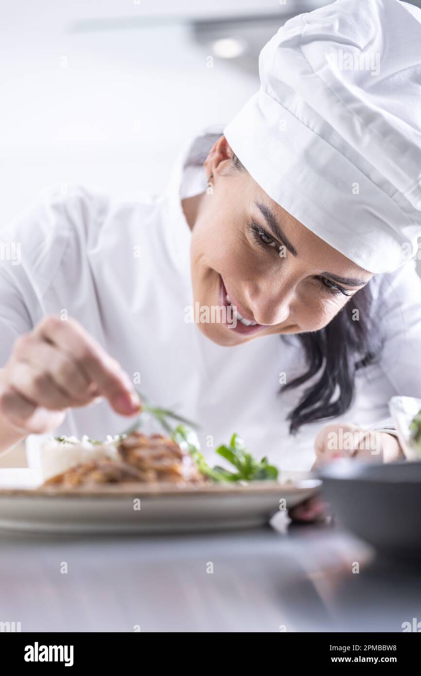 Eine junge Küchenchefin beendet das Essen mit Kräutern in der Restaurantküche - Nahaufnahme. Stockfoto