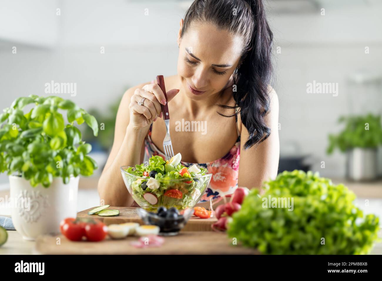 Gesunde Lebensweise junge Frau isst Salat. Junge Brünette, die in ihrer Küche gesundes Essen isst. Stockfoto