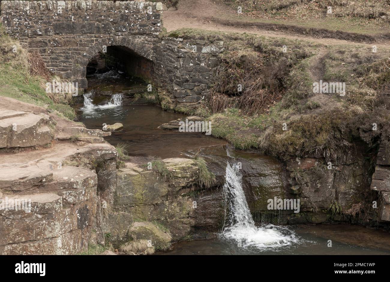 Wasser fließt an einem trockenen Tag unter einer alten Brücke über einen Wasserfall in einen Pool Stockfoto