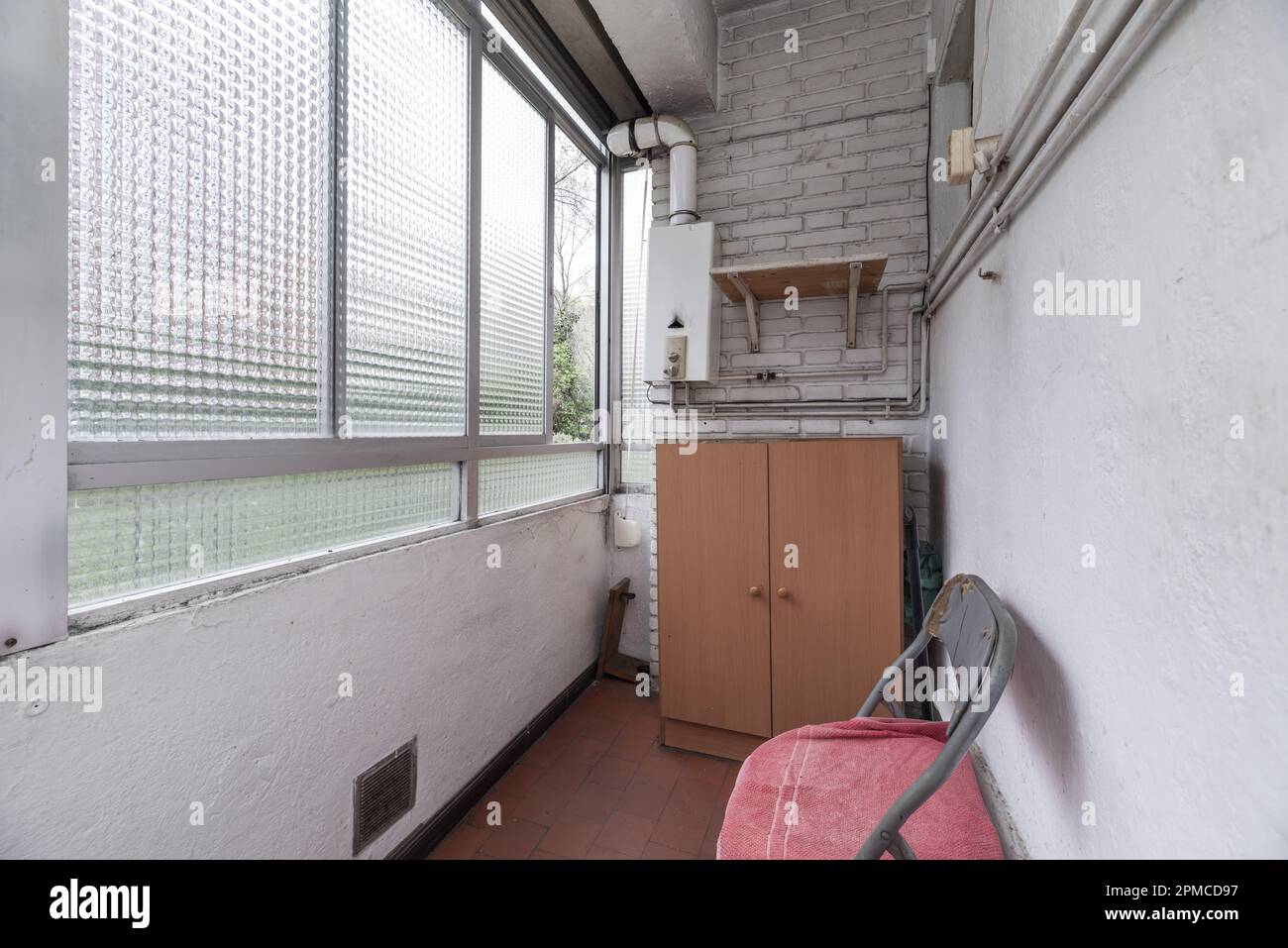 Eine kleine geschlossene Terrasse mit einem Glasfenster und einem Gasvorwärmer an einer weißen Backsteinwand Stockfoto