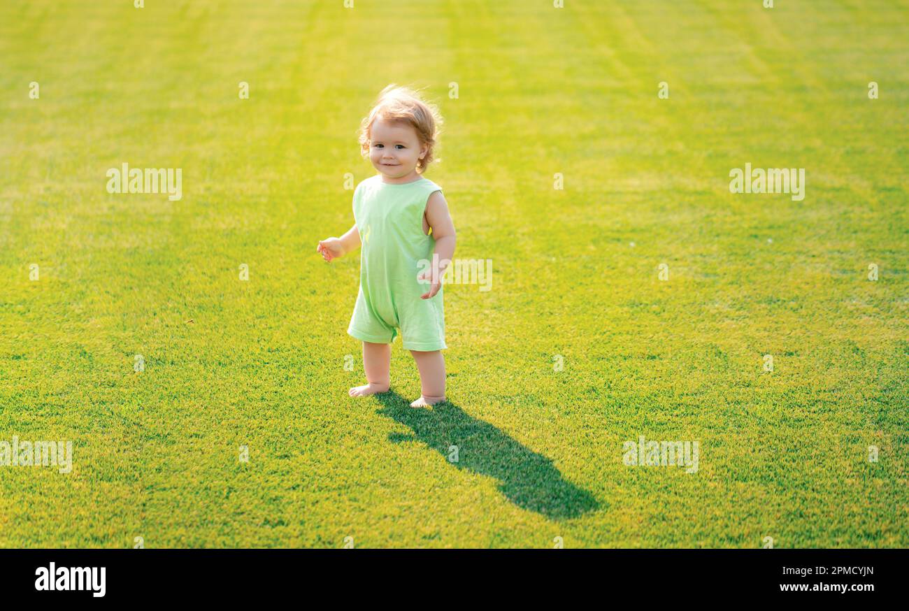 Baby steht barfuß auf dem grünen Rasen. Kleiner Junge, der im Sommerpark spielt. Glückliche Kindheit und Kinderpflege. Stockfoto