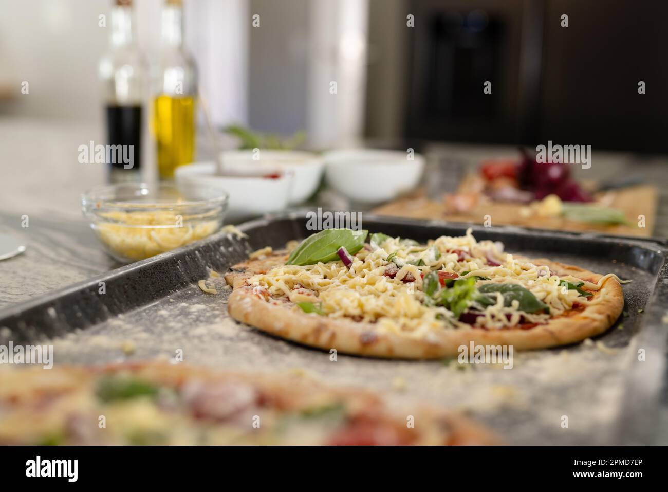Nahaufnahme von Pizza garniert mit Kräutern und Käse in einem Tablett über der Kücheninsel zu Hause Stockfoto