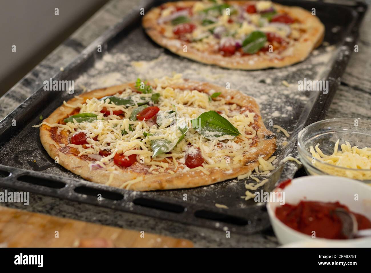 Aus einem hohen Winkel gefertigte Pizza, garniert mit Kräutern und Käse in einem Tablett über der Kücheninsel zu Hause Stockfoto