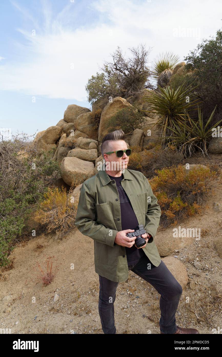 Männlicher Tourist mit Sonnenbrille in Schwarz mit grüner Jacke und Kamera in Joshua Tree, Kalifornien. Stockfoto