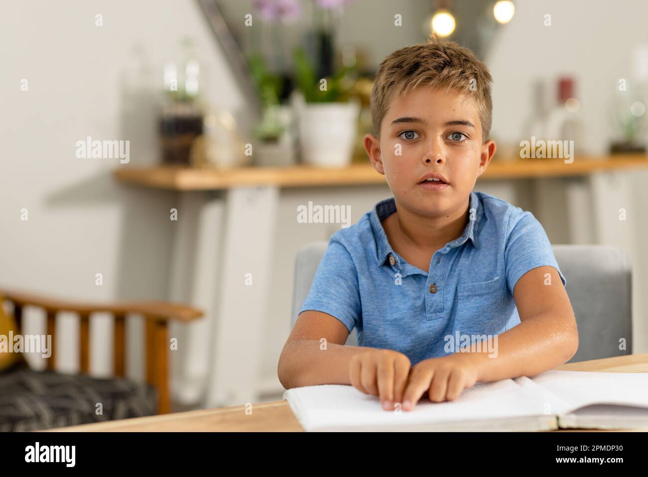 Porträt eines weissen blinden Jungen, der auf dem Tisch ein Braillenbuch liest, während er zu Hause sitzt, Kopierraum Stockfoto