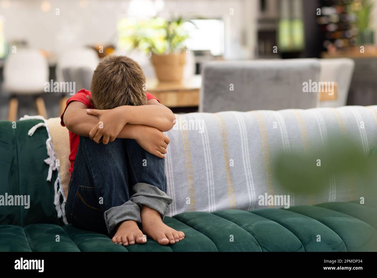 Ein trauriger, weißer Junge, der sich in den Knien umarmt, während er im Wohnzimmer auf dem Sofa sitzt, Kopierraum Stockfoto