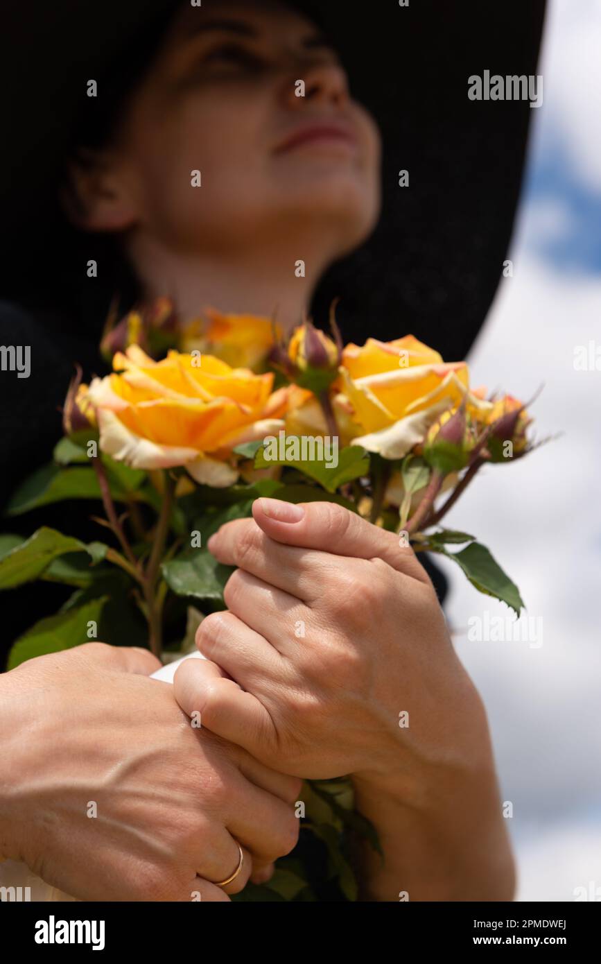 Strauß gelber Rosen in den Händen einer verheirateten Frau mit Hut, Blick von unten, selektiver Fokus. Stockfoto