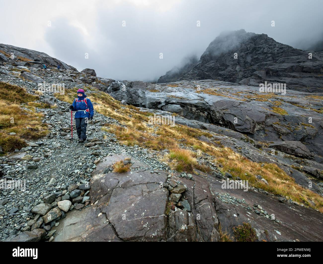 Bergwanderin in nasser Wetterausrüstung, die bei schlechtem Wetter von Coire Lagan in den Black Cuillin Bergen auf der Isle of Skye, Schottland, Großbritannien, absteigt Stockfoto