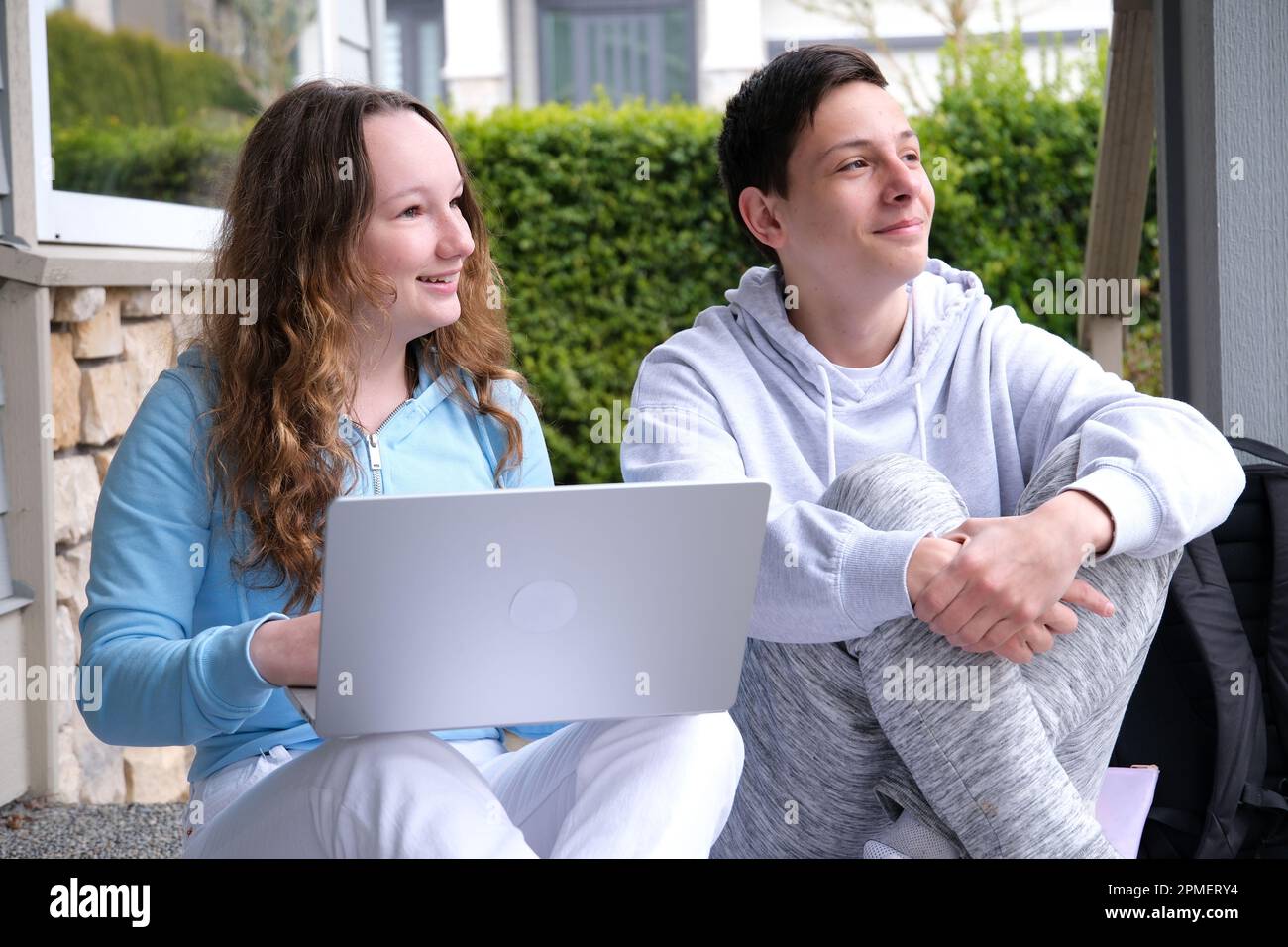 Die erste Liebe, junge Teenager-Liebhaber-Paare lernen Laptop, Junge und Mädchen machen Hausaufgaben, erstes Date, Blumen und Kinder lieben. In weißen Kleidern sitzen Teenager nach der Schule auf der Veranda und schauen in die Hände in eine Richtung Stockfoto