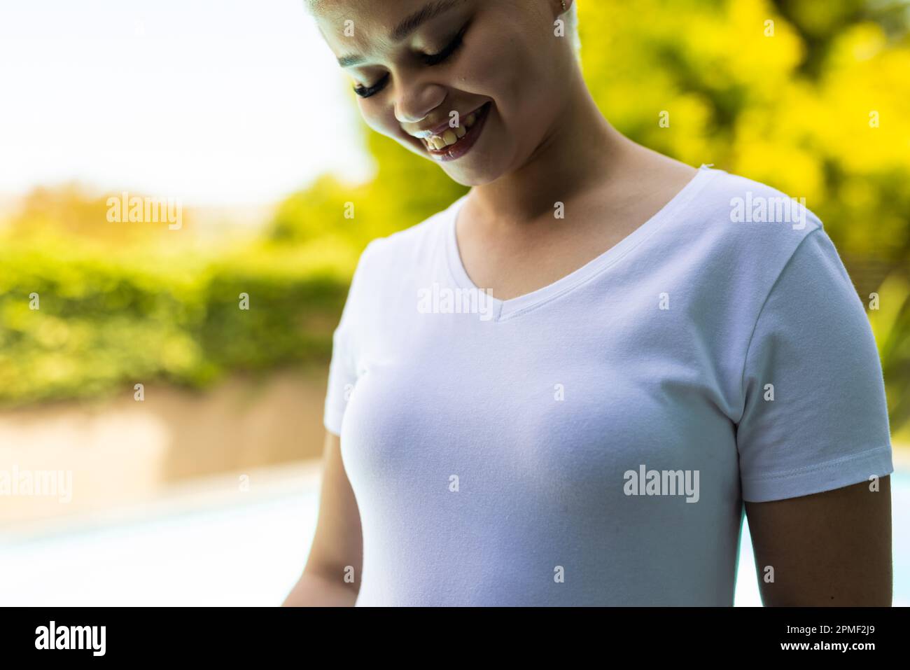 Eine glückliche, birassische Frau, die ein weißes T-Shirt über dem Pool im Garten trägt Stockfoto