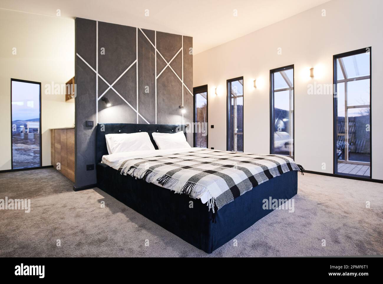 Minimalistisches Interieur des Schlafzimmers mit großem Bett drinnen. Vorderansicht des breiten Bettes mit karierter Decke an der grauen Wand mit geometrischen Verzierungen im Schlafbereich. Innenkonzept. Stockfoto